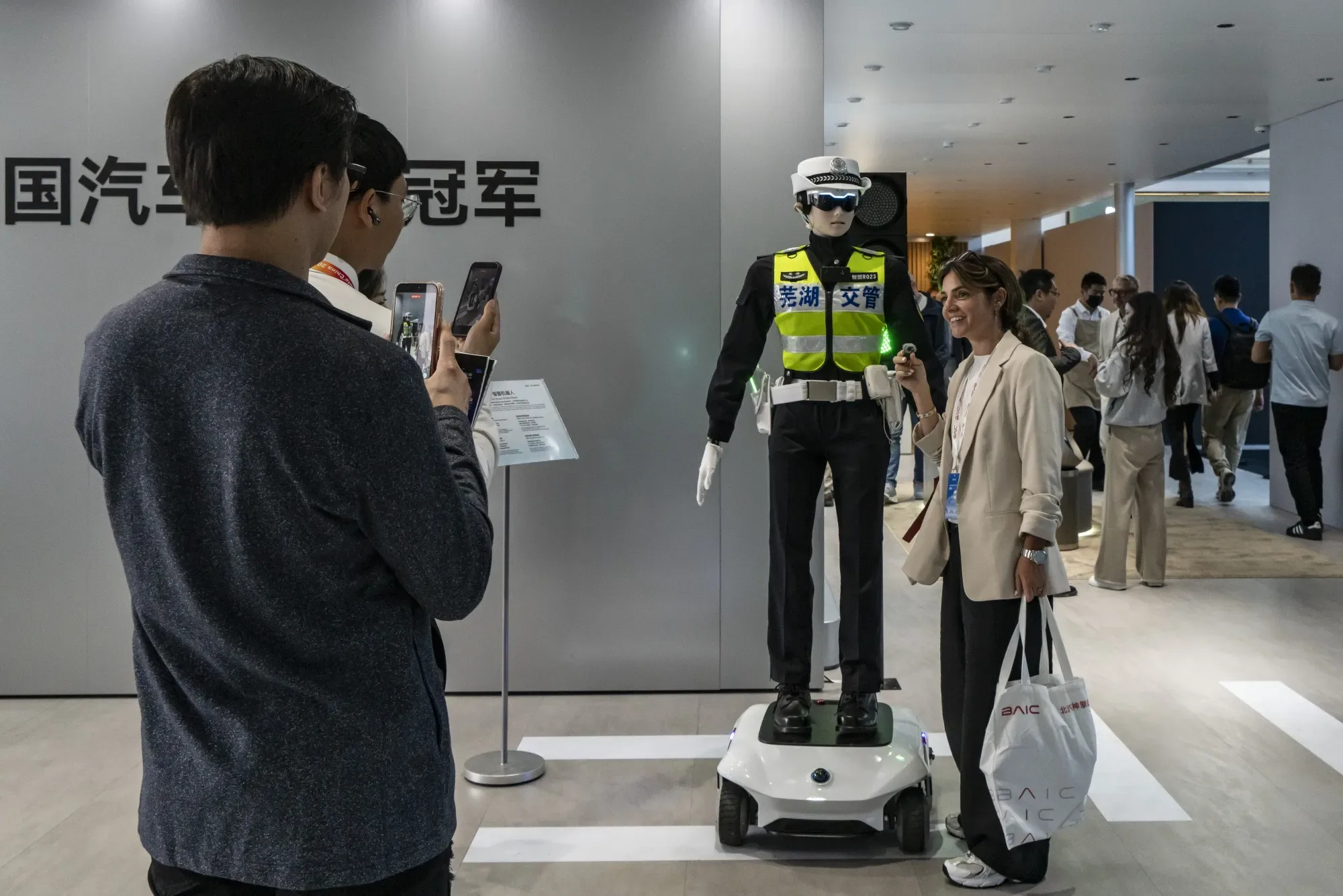 Robô humanóide vestido de guarda de trânsito chinês em exposição tecnológica, com visitantes tirando fotos ao lado da máquina