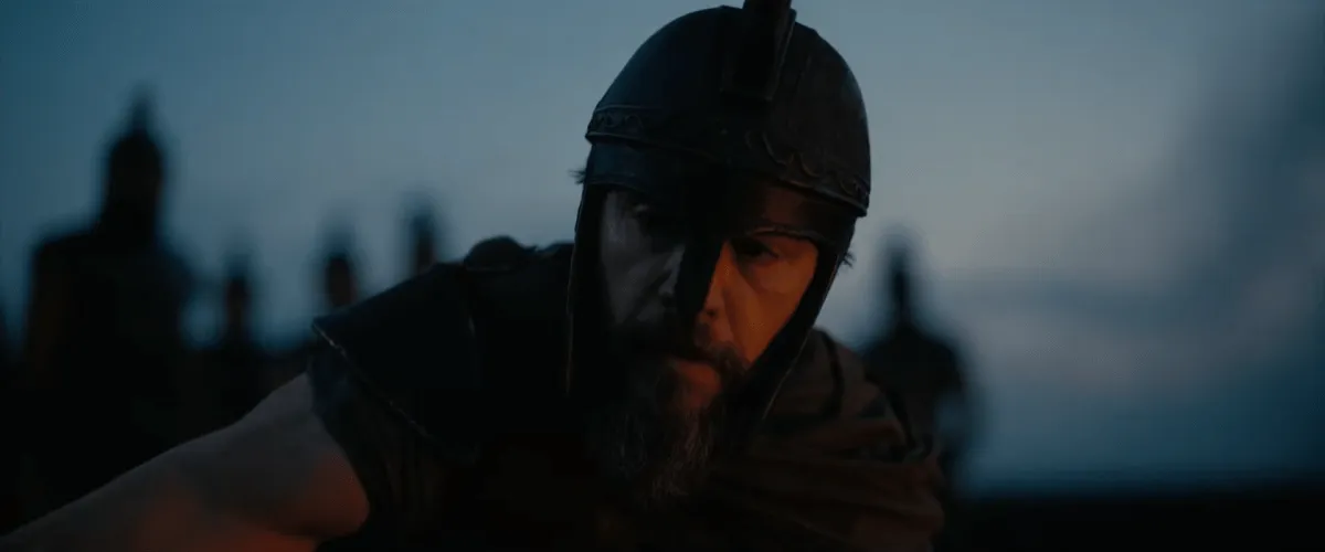 Matt Damon como Ulisses, de capacete e armadura de bronze, em cena de A Odisseia de Christopher Nolan ao entardecer
